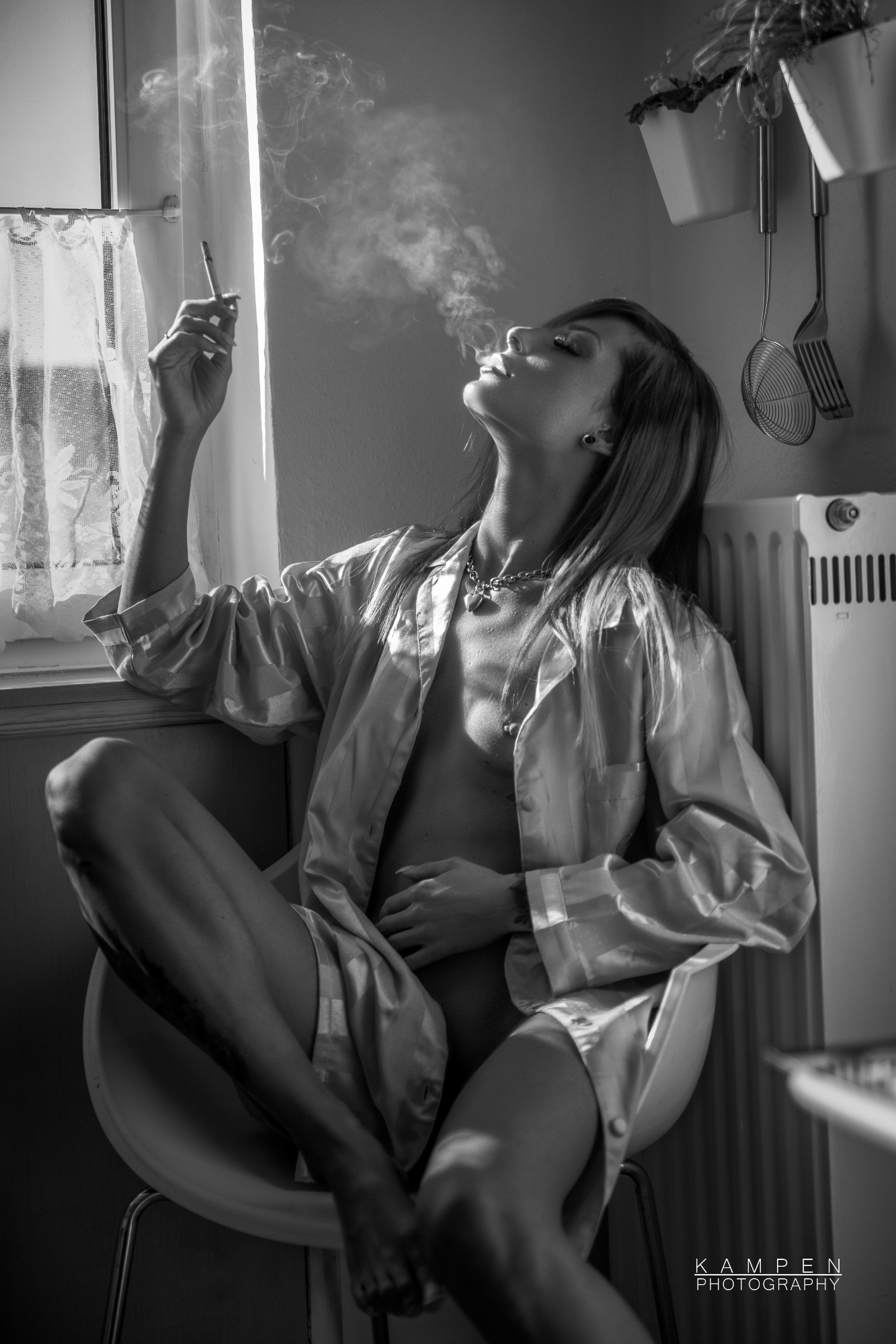 PIcture are in black and white. A female are sitting in what appears to be a kitchen and smoking